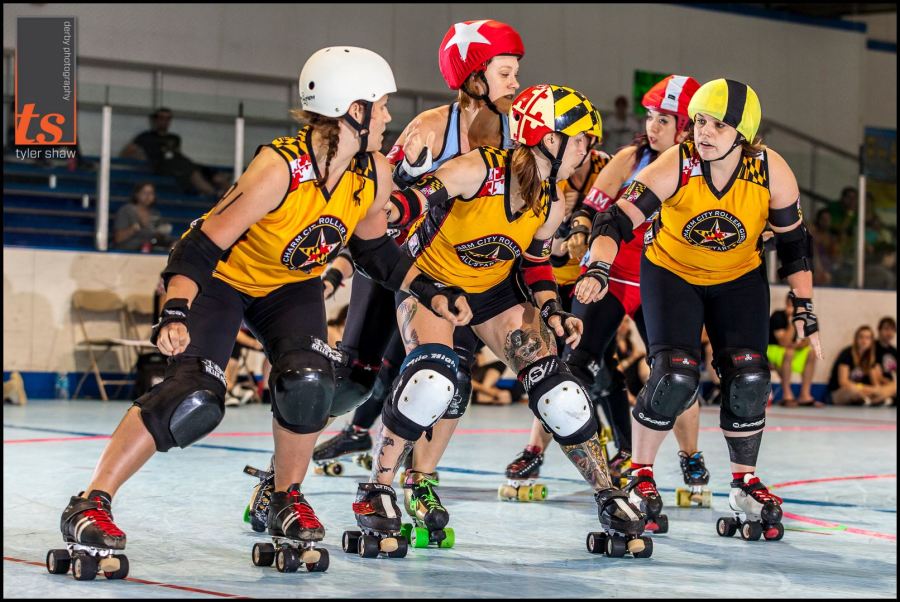 Holly Go Hardly doesn't need to snap her head back & forth to know where her opponent is. She keeps her head steady, and sits on her opponent to feel her movement. Notice how the inside & outside line blockers are looking? Wonderful! Photo by Tyler Shaw - Prints Charming Derby Photography